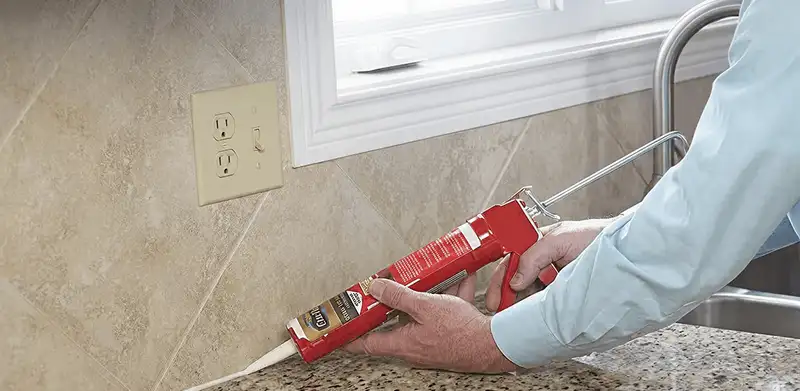 Handyman applying caulk along a kitchen backsplash and countertop seam in Tallahassee, FL