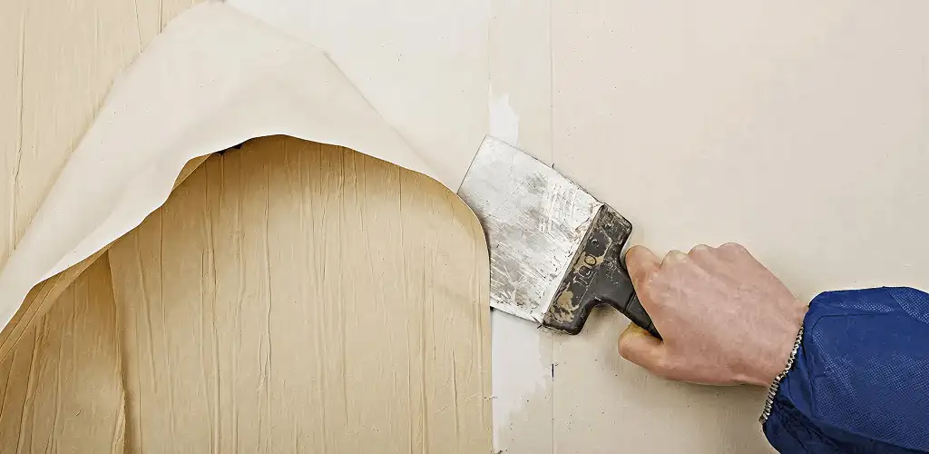 Handyman removing wallpaper with a scraper for wall preparation in Tallahassee, FL
