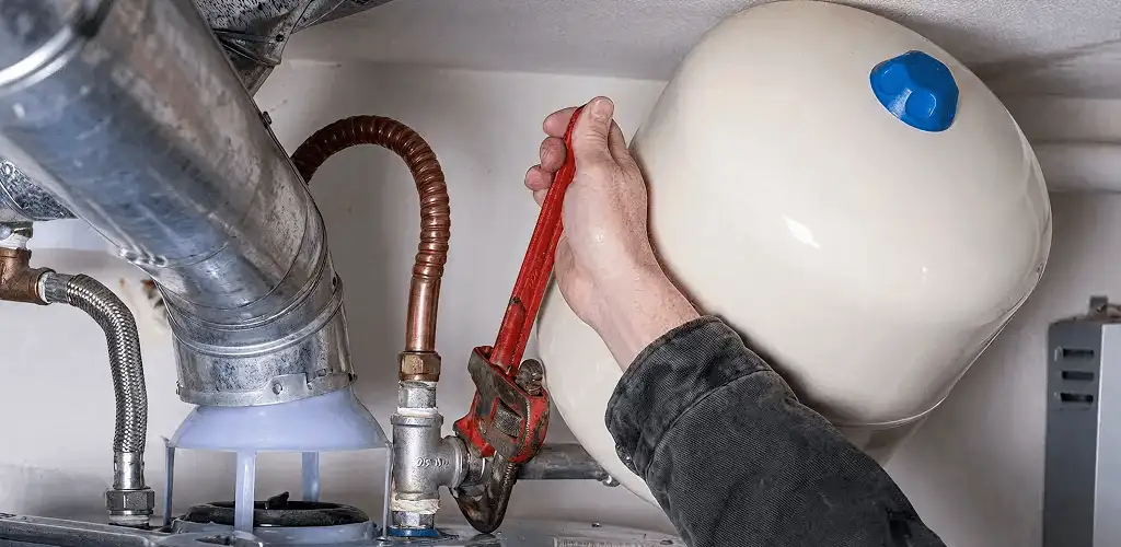 Water heater repair technician tightening plumbing connections near a tank unit in Tallahassee, FL